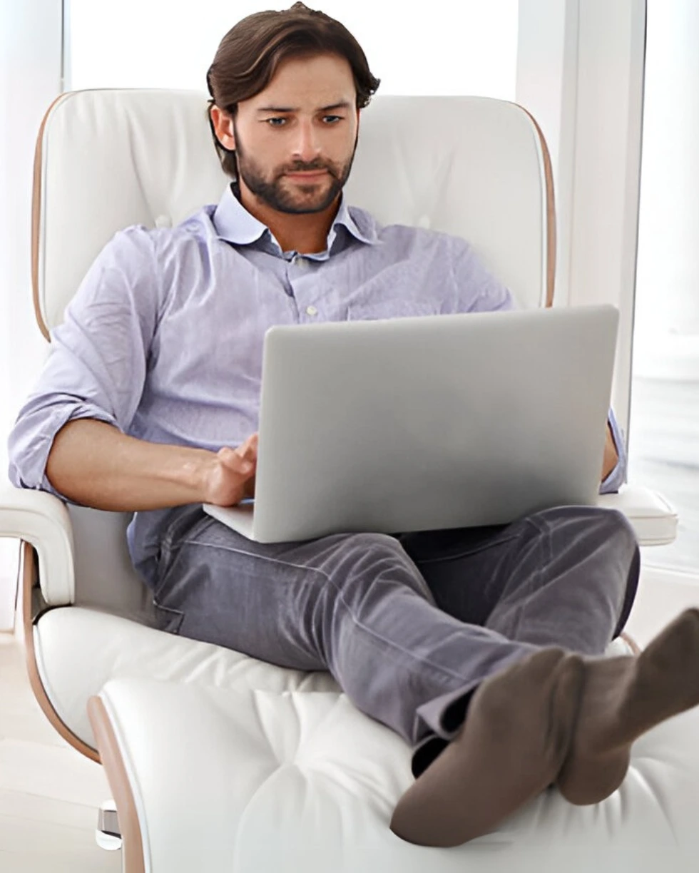 Man working on laptop while sitting on a modern white recliner chair