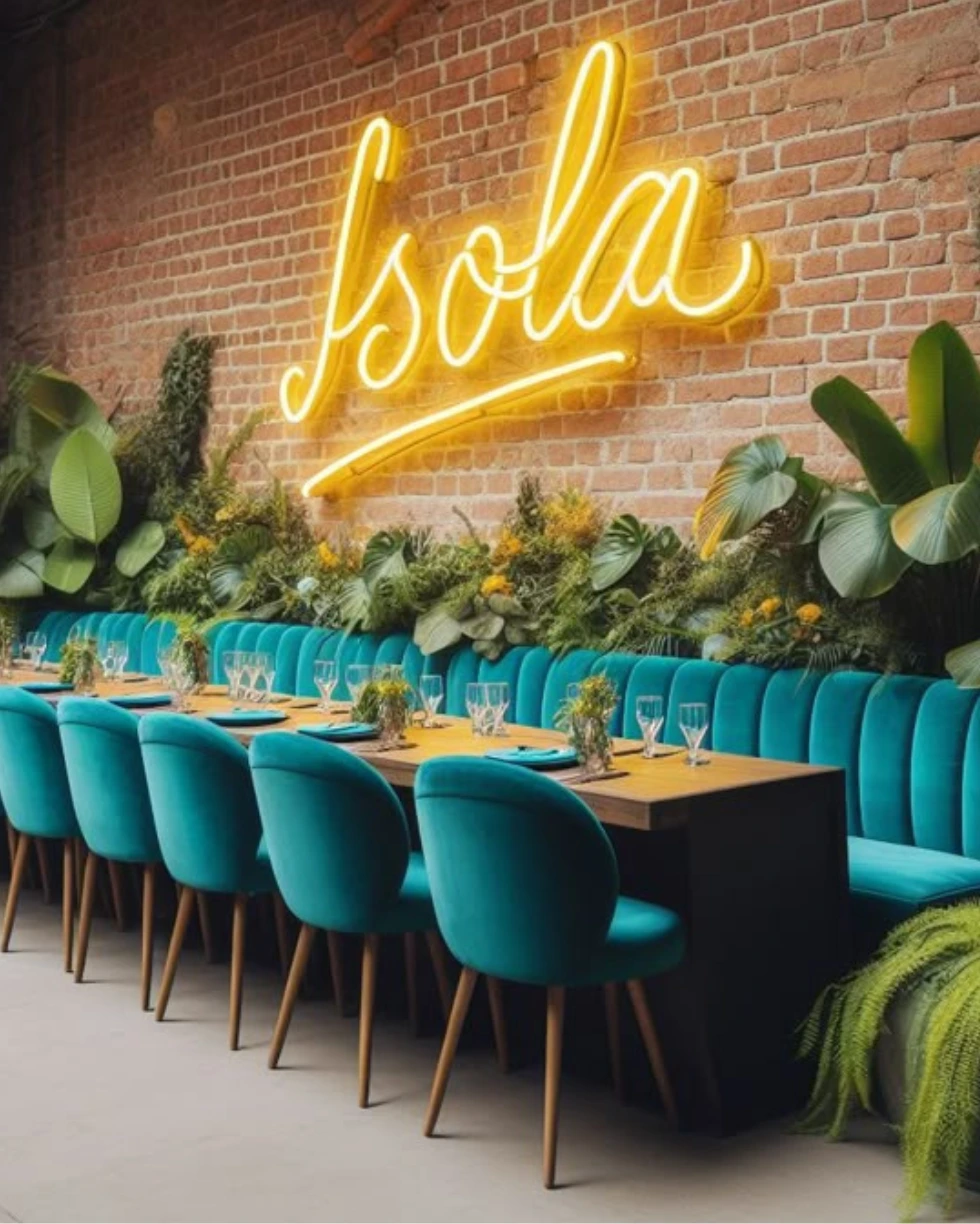 Trendy restaurant with teal velvet chairs, brick wall, and neon Isola sign