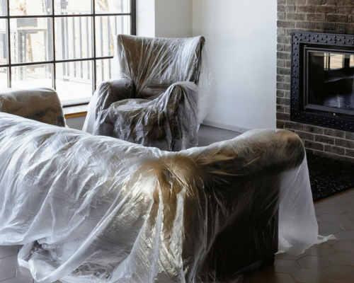 Living room furniture covered in plastic protective sheets near fireplace