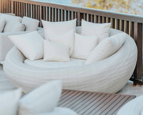 Round white wicker outdoor lounge chair with multiple white cushions on a wooden deck