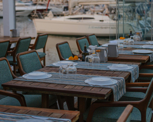 Outdoor dining setup with wooden tables and green chairs by the marina