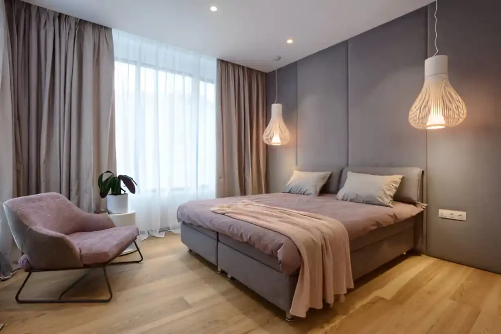 Modern bedroom with grey walls, double bed, pendant lights, and cozy pink armchair